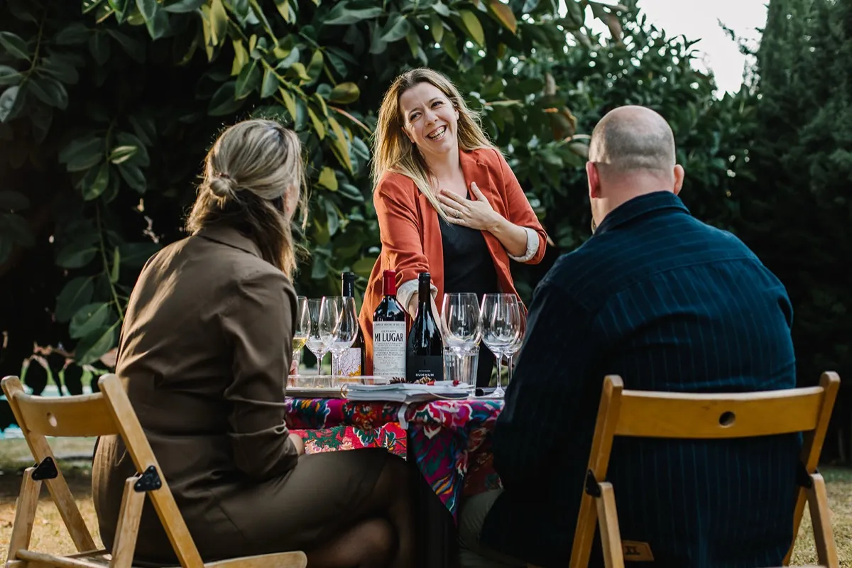 Linda from Winederlust laughing with two guests across a table of wine bottles and glasses at a private tasting in a Málaga garden. Photo courtesy of Winederlust
