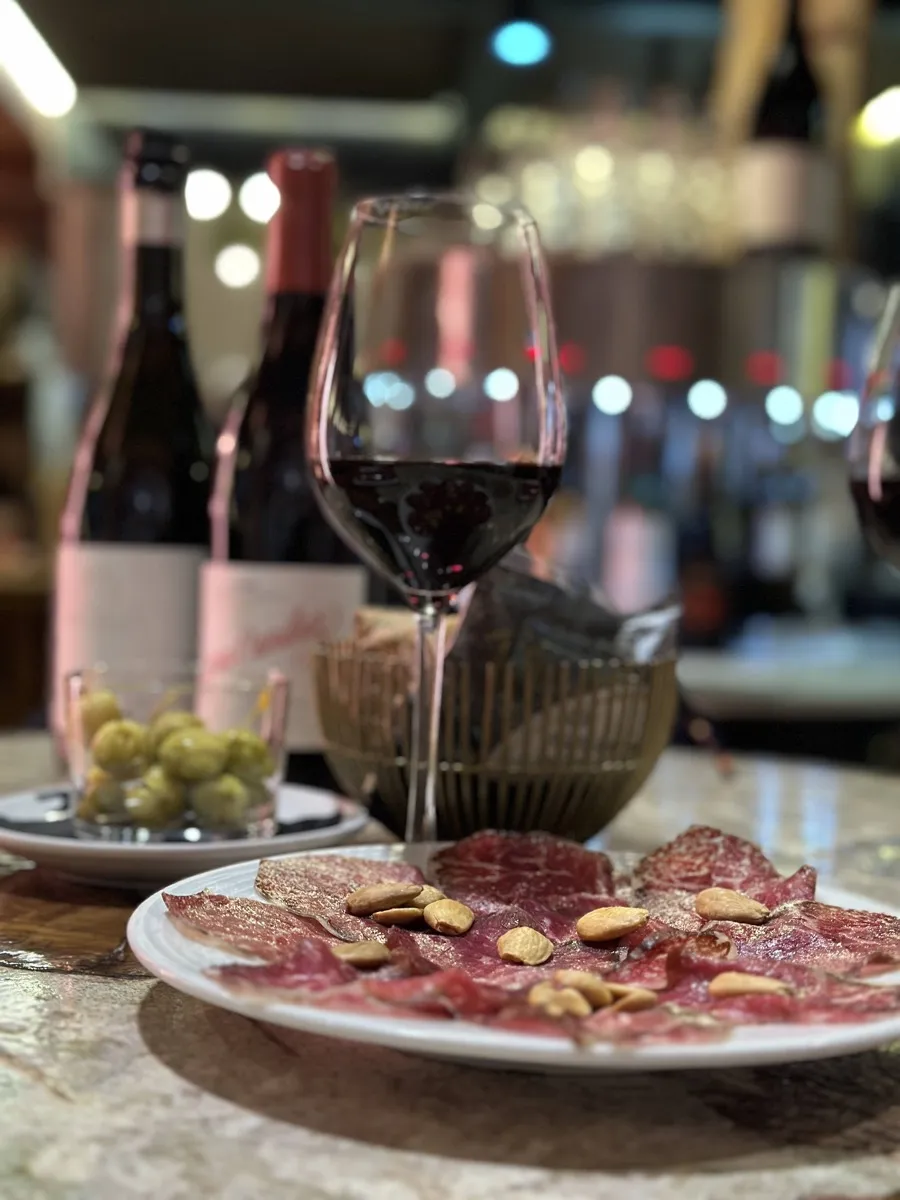 A glass of red wine beside two bottles, a bowl of olives and a plate of cured meat with almonds on a bar counter in Málaga. Photo courtesy of Winederlust