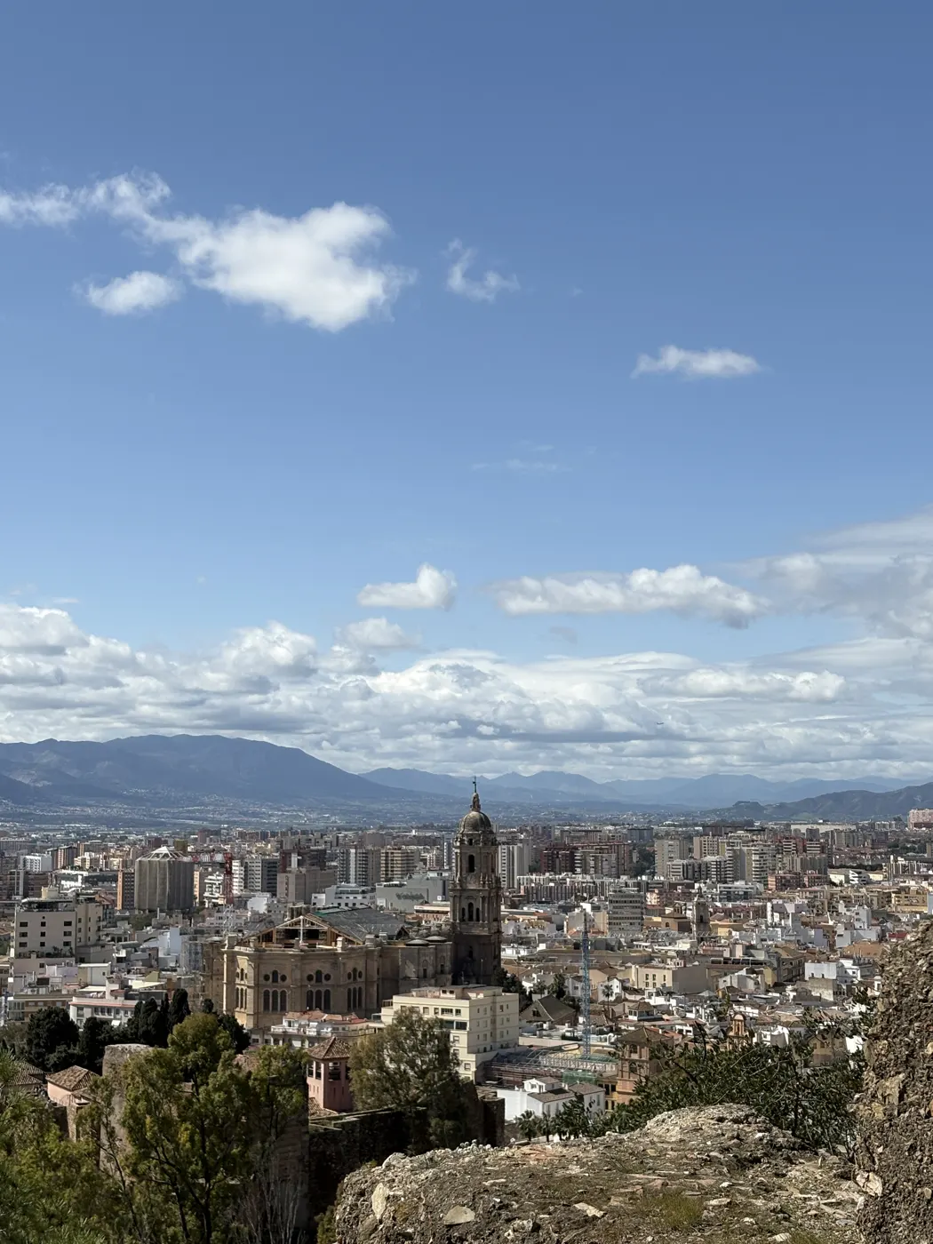 Elevated view over Malaga's rooftops and the Cathedral tower from a hilltop, with the city sprawling out toward the mountains