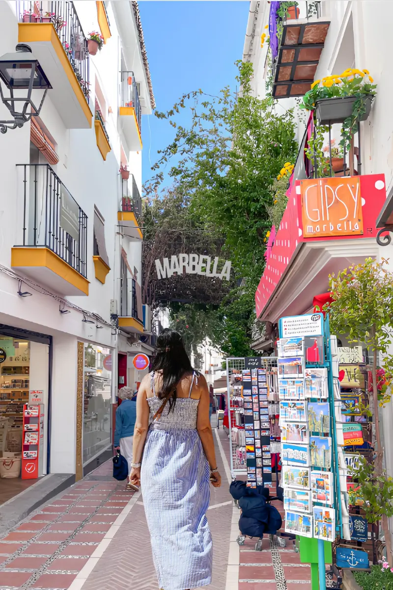 Heidi walking down Calle Nueva in Marbella beneath the white MARBELLA sign