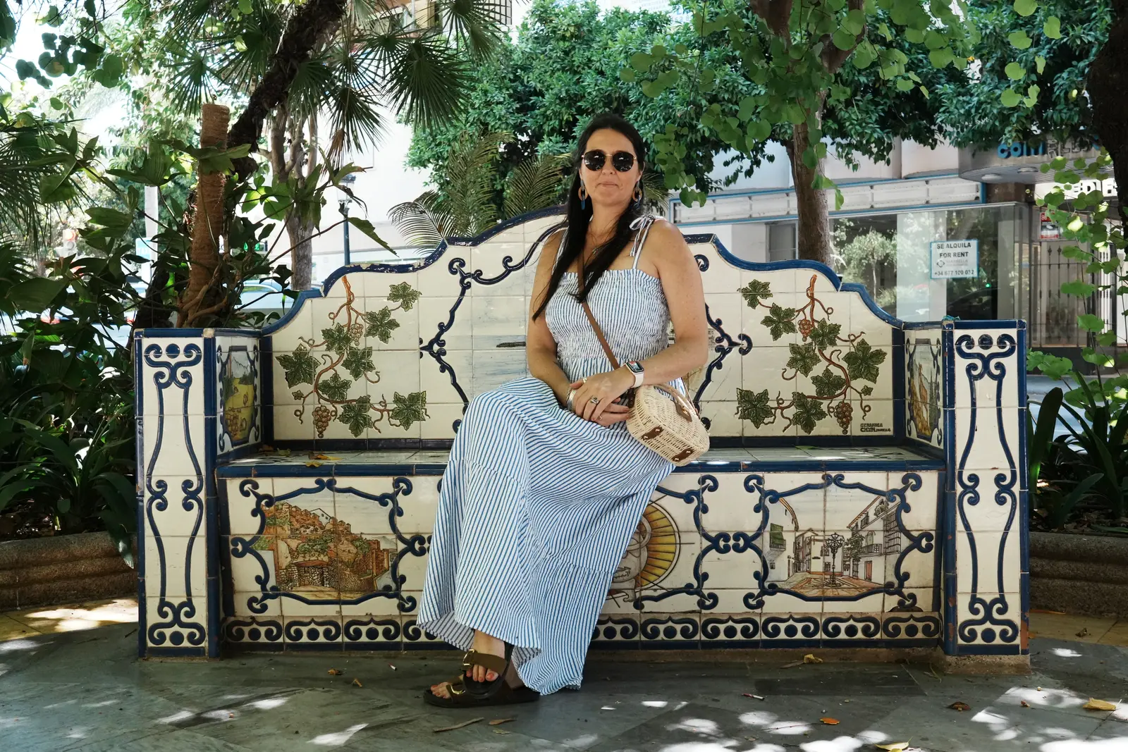 A woman sitting on a ebautiful tiled chair in a prak in Marbella.