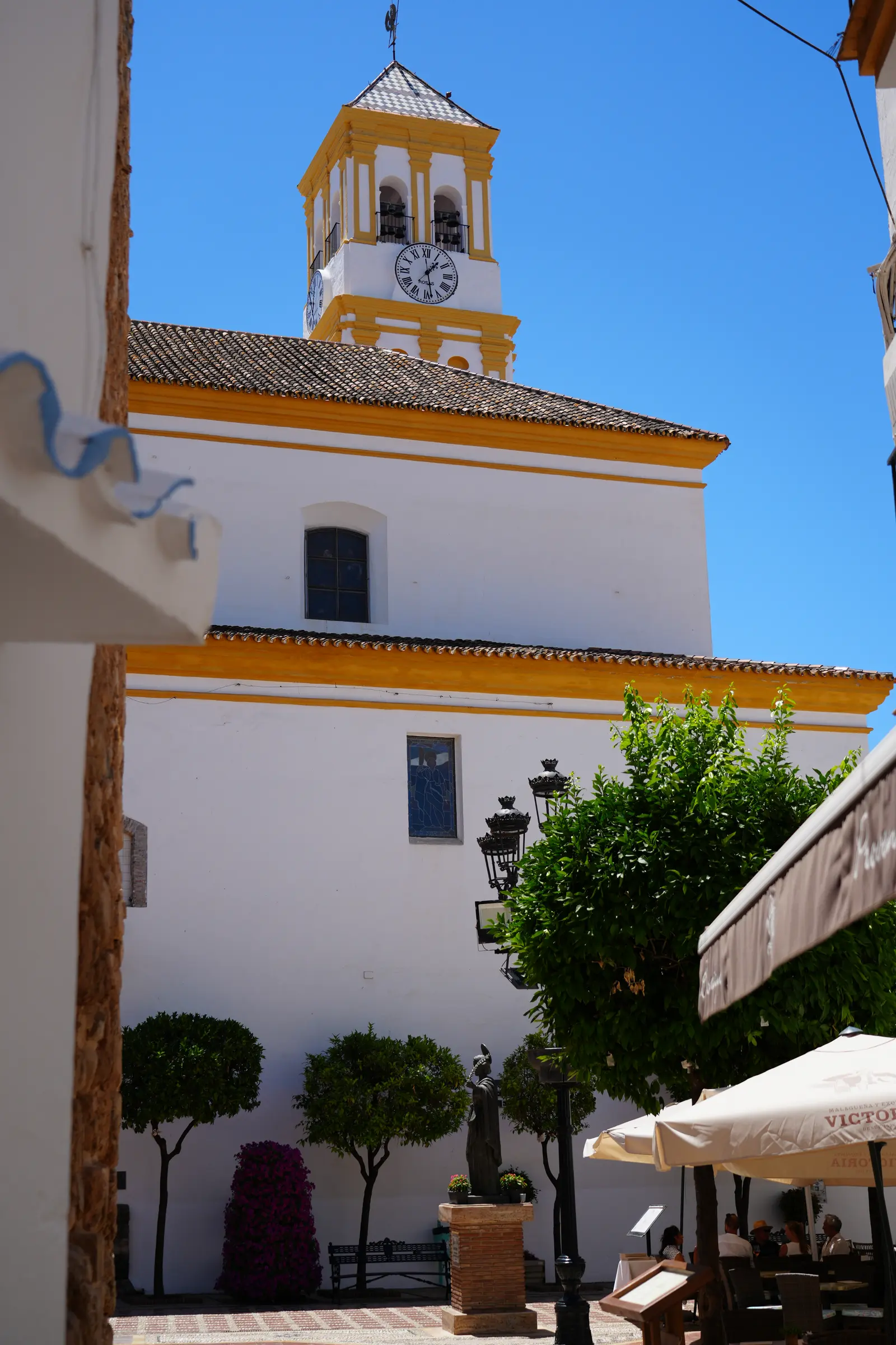 The white and yellow bell tower of the Iglesia de la Encarnacion in Marbella, with its Roman-numeral clock face and tiled spire