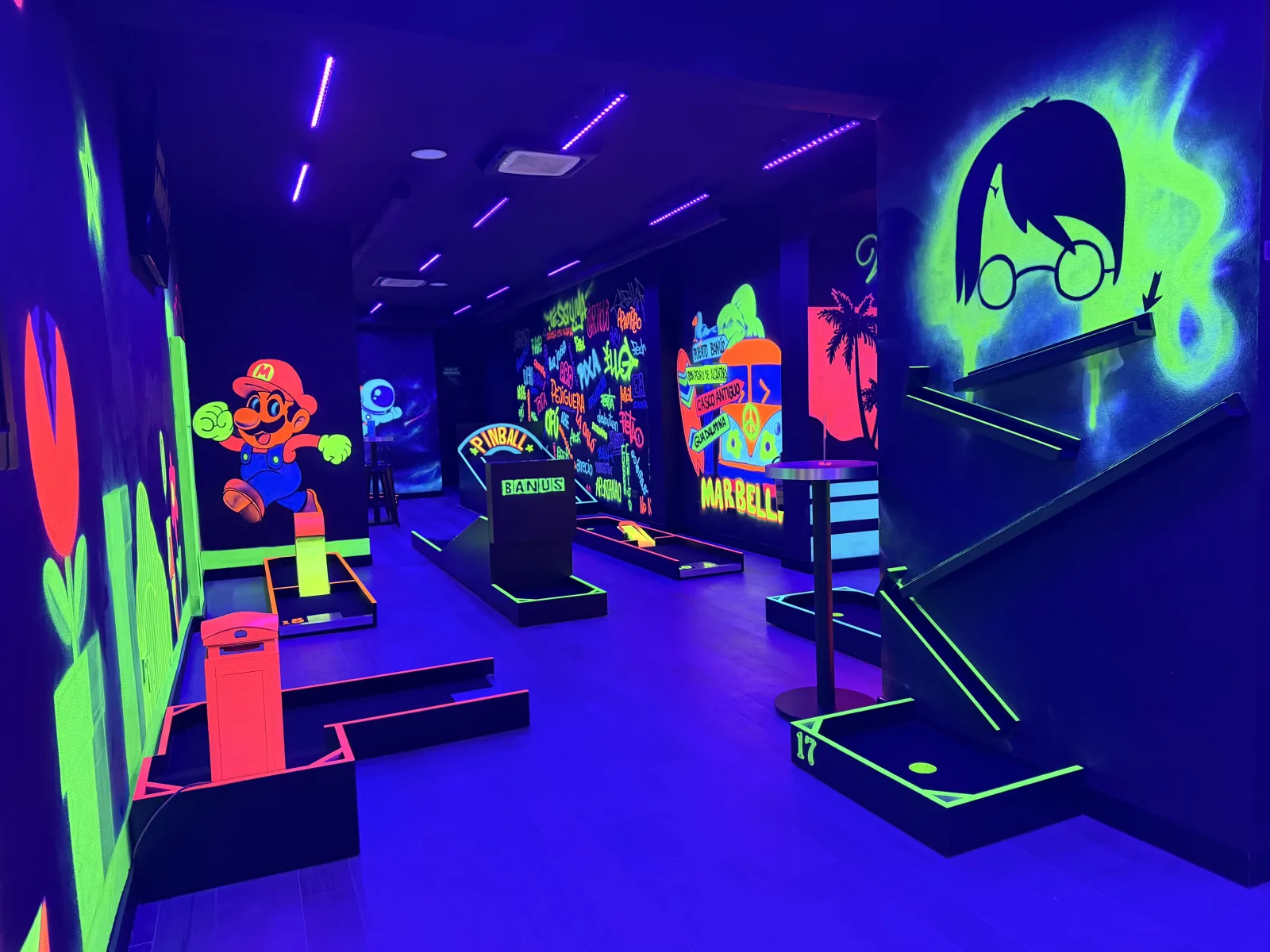 Neon UV-lit indoor minigolf course in Marbella, with glowing murals of Puerto Banús and Marbella old town running along the wall