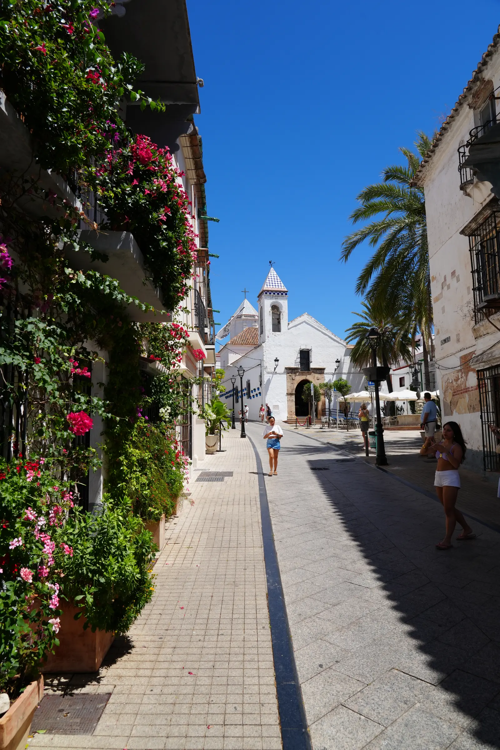 Cobblestone street in the heart of Marbella old town with a white church in the distance.