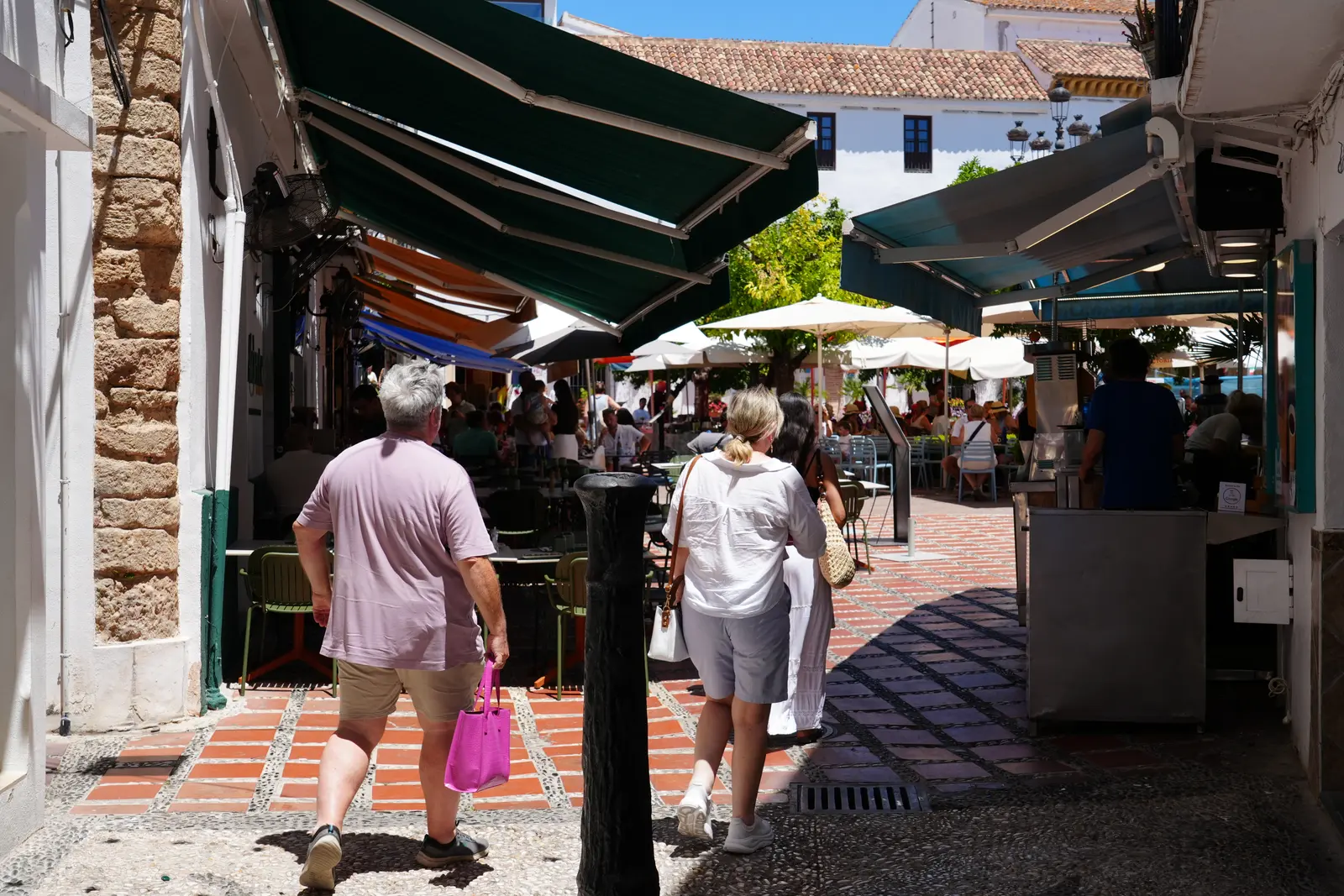 people walking in he streets of marlbella white washed walls and canopys for the sun.