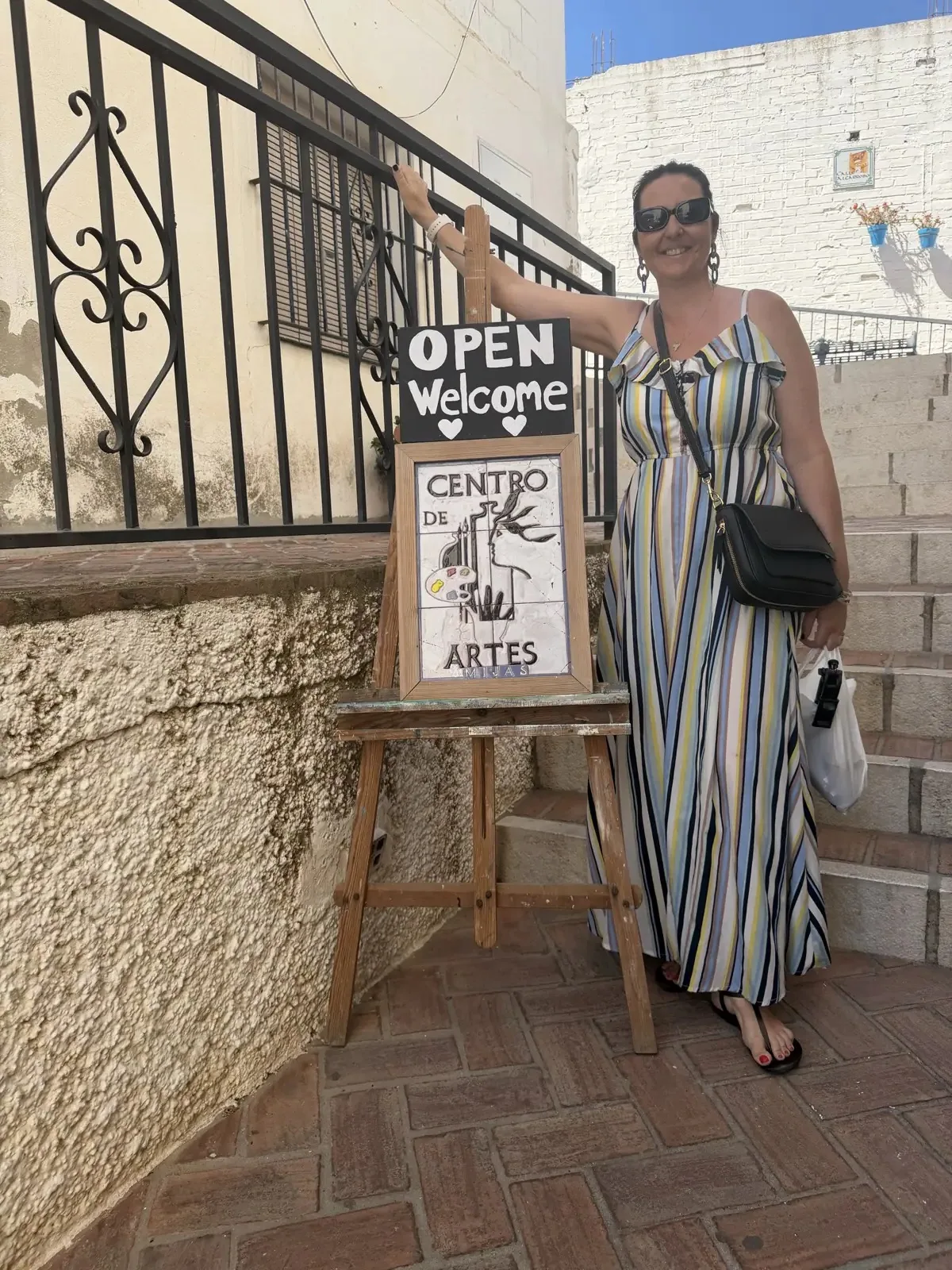 Woman posing beside the Centro de Artes entrance sign in Mijas Pueblo