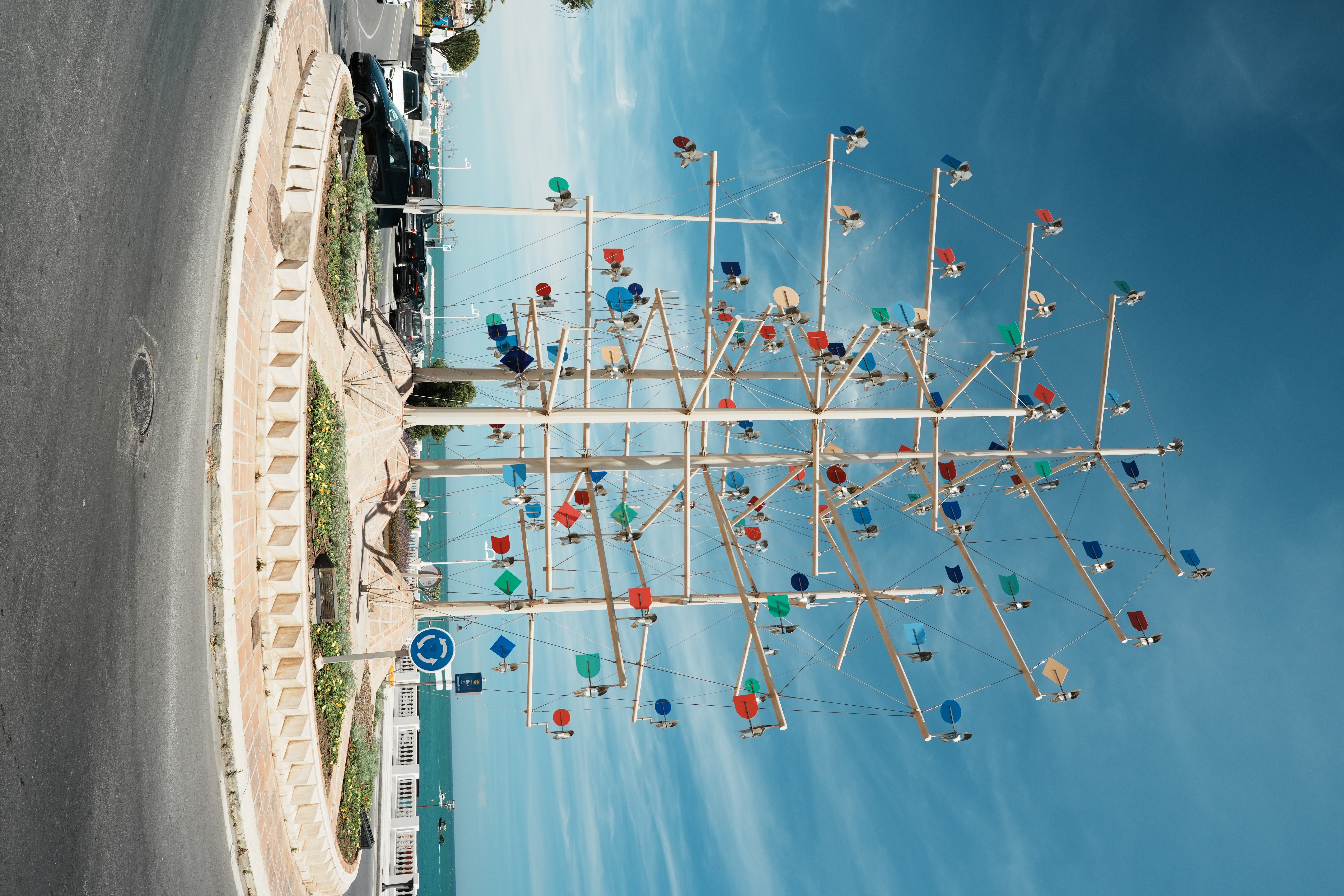 Colourful kinetic wind sculpture on a roundabout in Benalmadena, with the marina behind