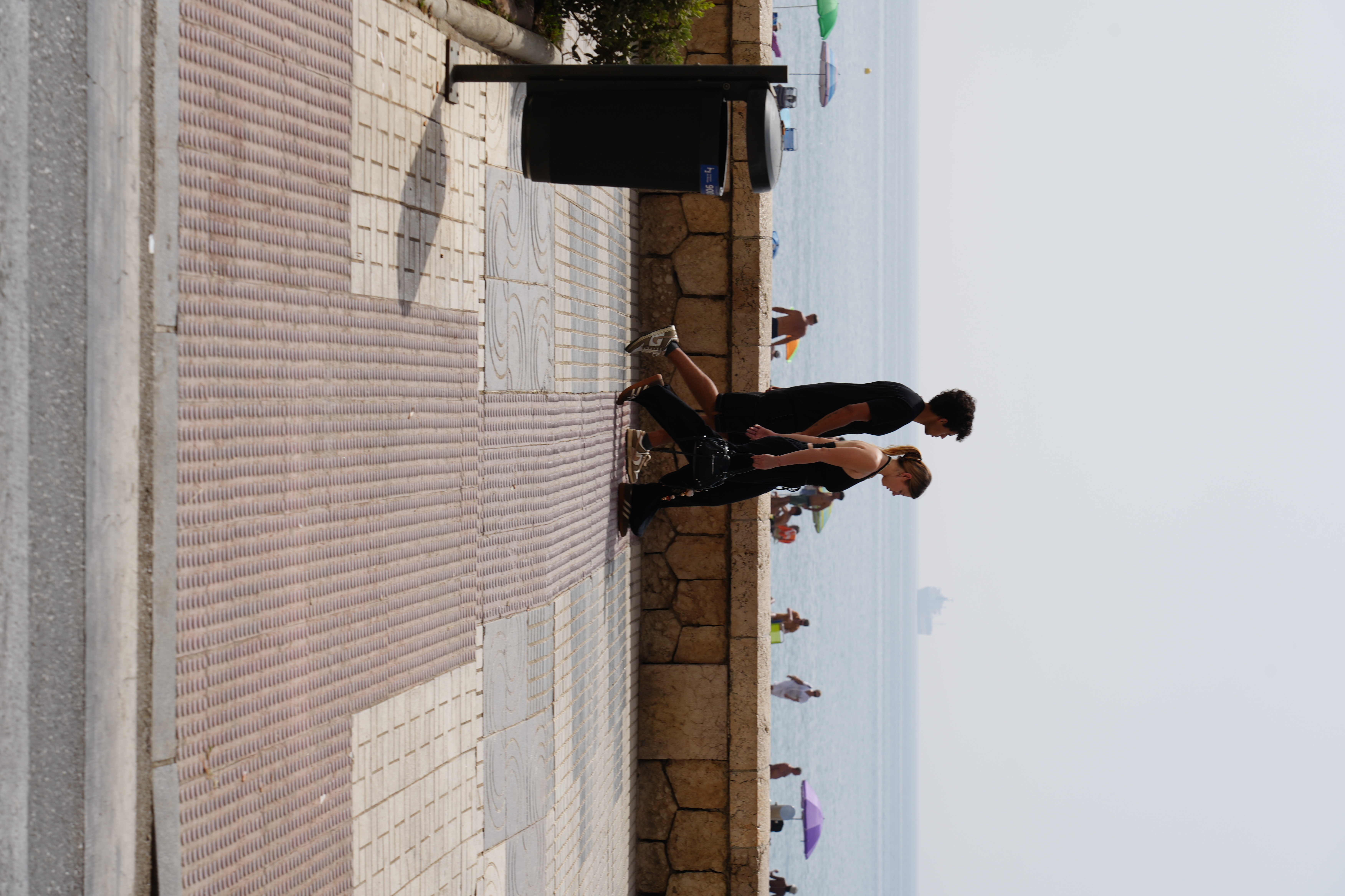 Joggers on the beach promenade in Malaga, with sunbathers on the sand behind