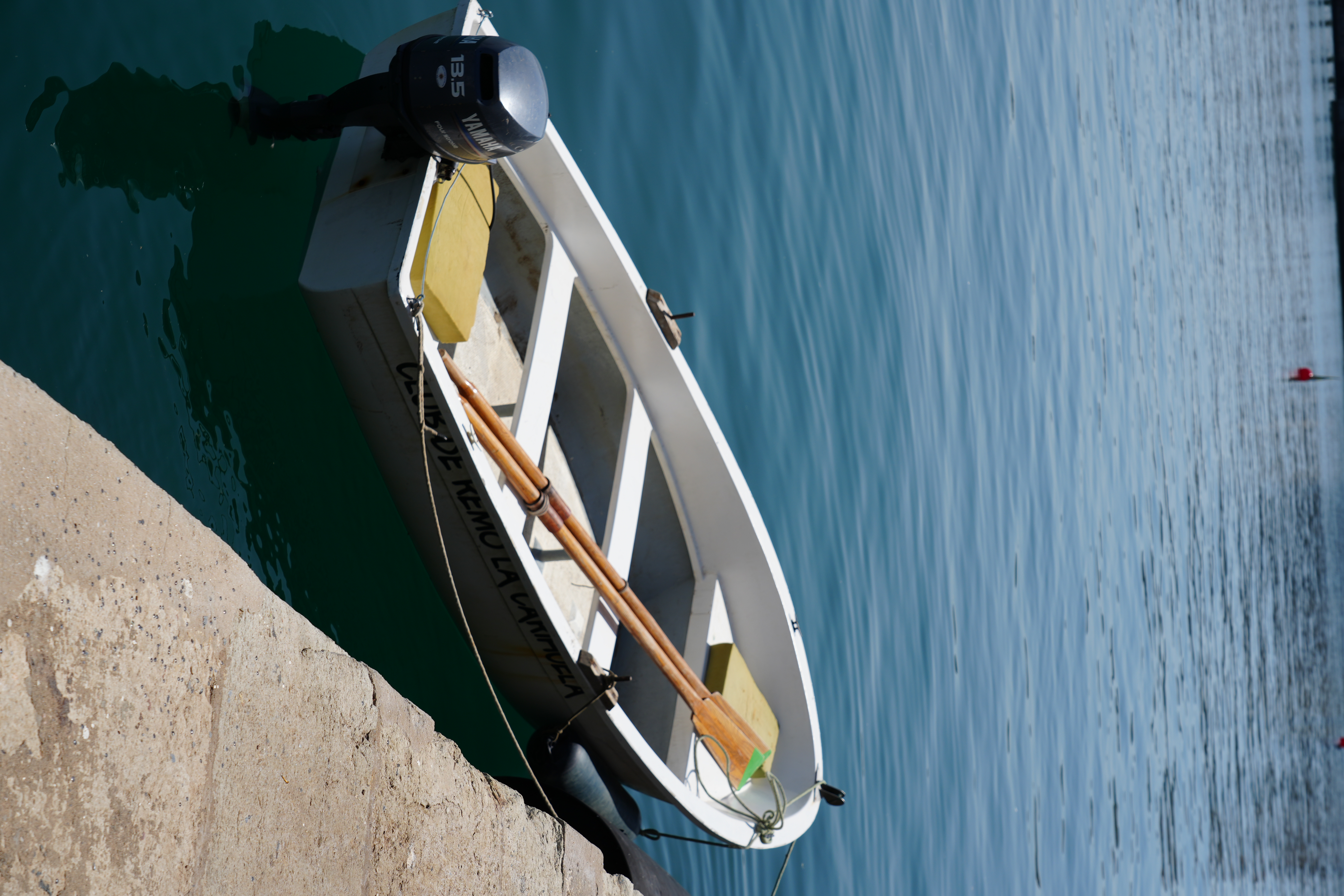 A small rowing club boat moored against the harbour wall in Malaga