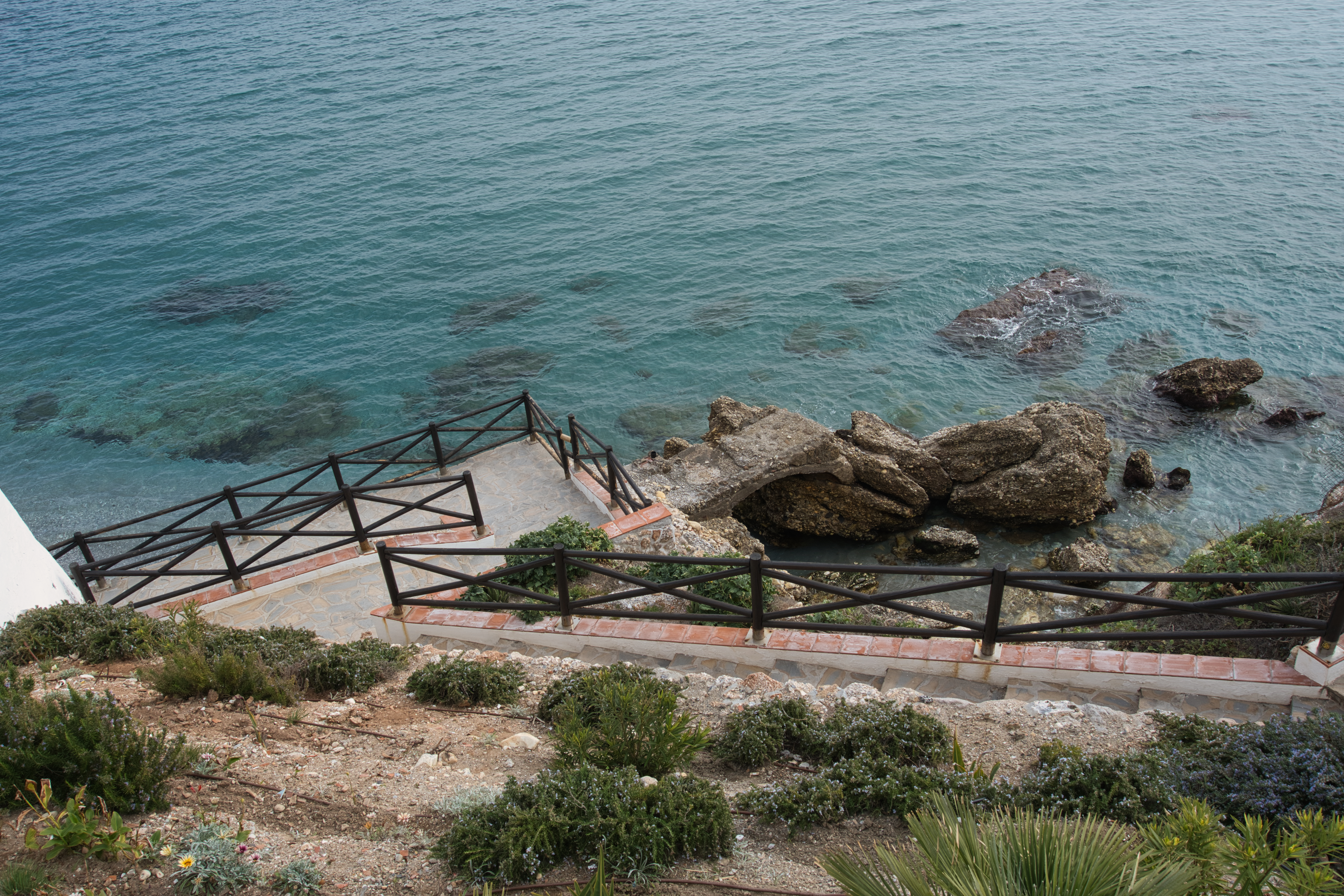 A staircase leading down to the rocky shoreline and turquoise water in Nerja