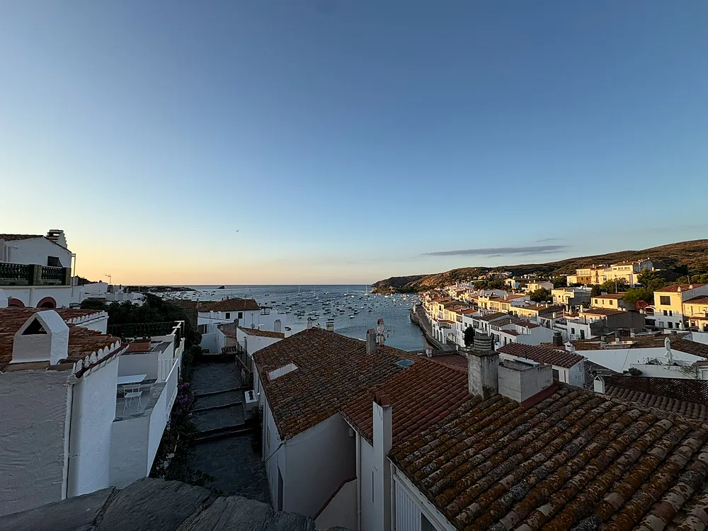 Terracotta rooftops and whitewashed houses of Cadaqués looking down a stepped lane to the harbour and moored boats at dusk