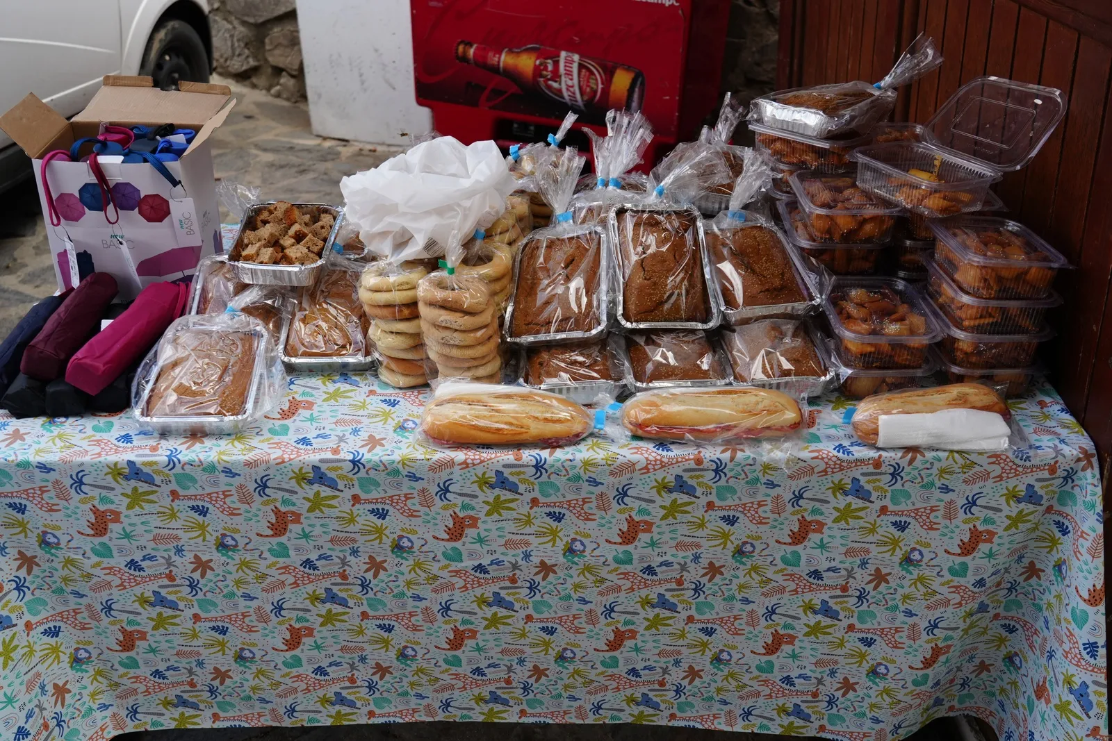 A stall table covered in a floral cloth, piled with home-baked cakes and bread wrapped in plastic