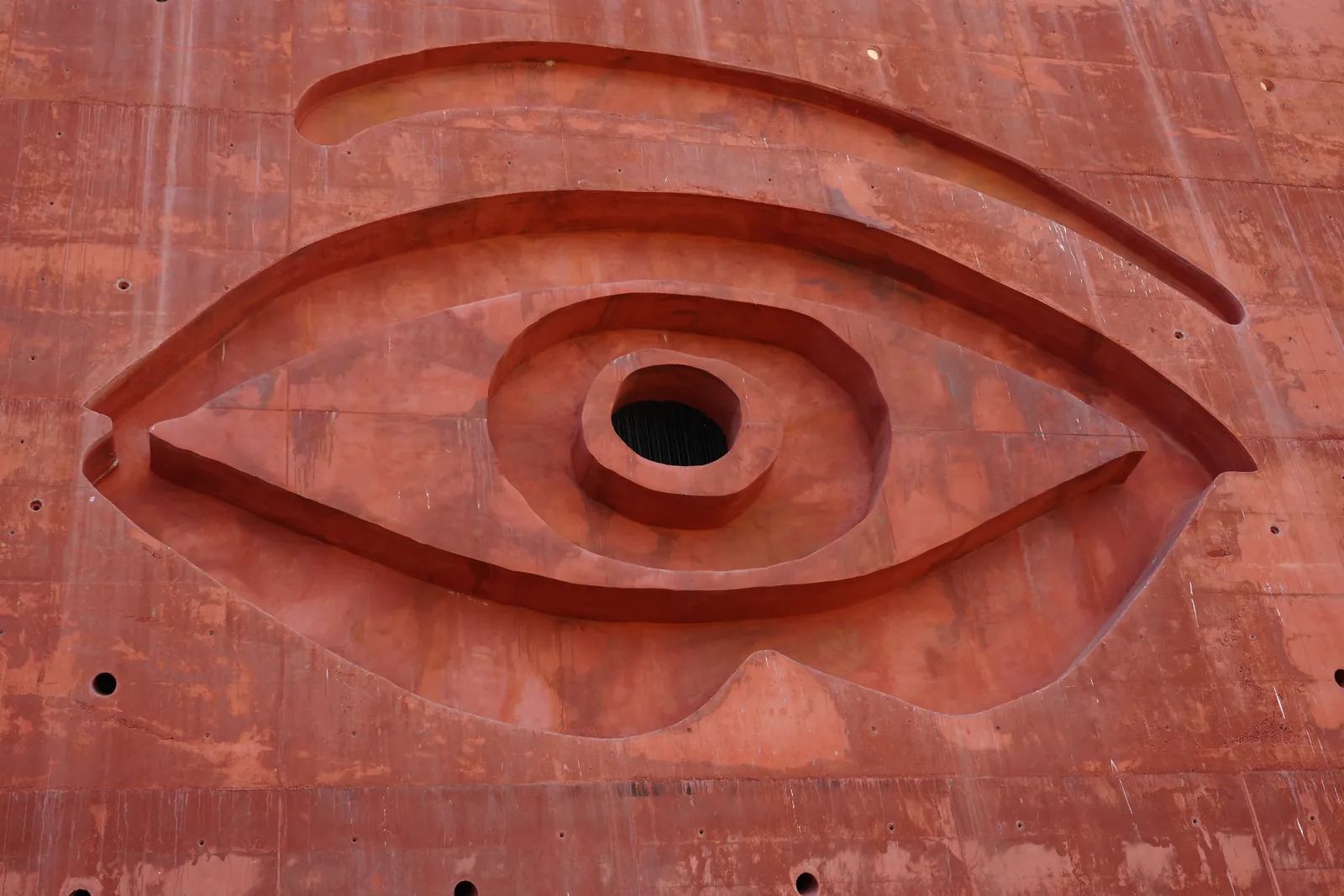 Close-up of the giant eye carved into the red wall of LA Almazara, with a round hole as the pupil
