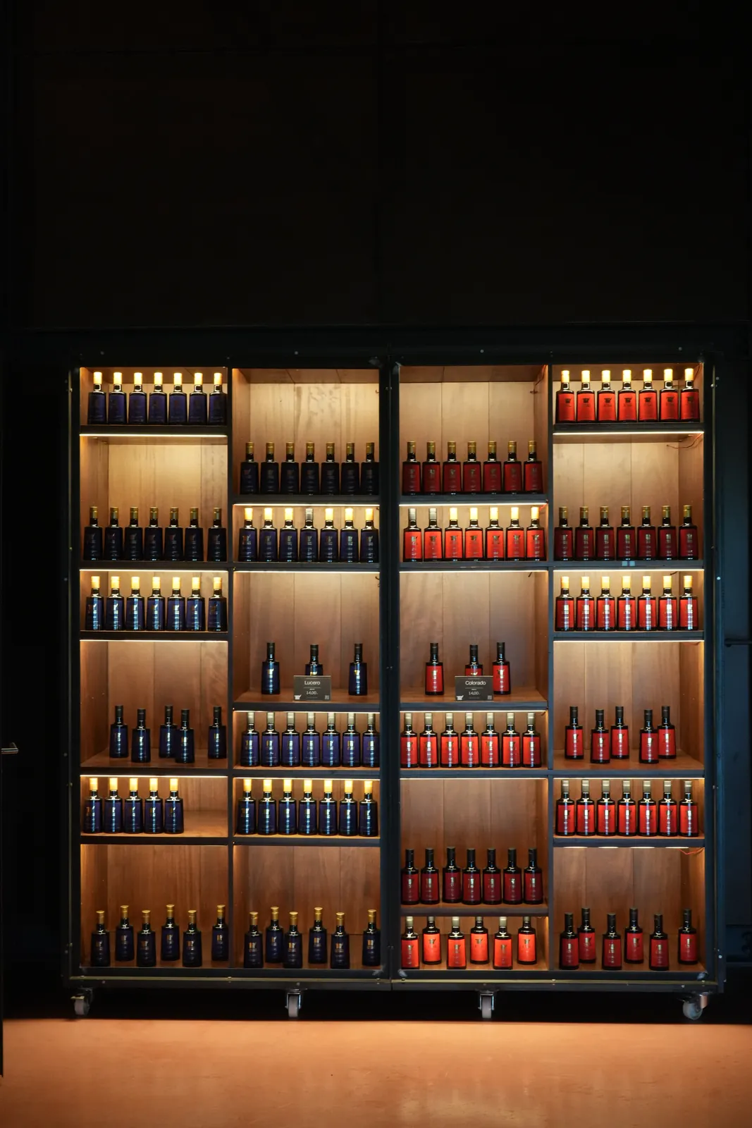 Lit shelves of blue and red olive oil bottles in the dark main hall at LA Almazara