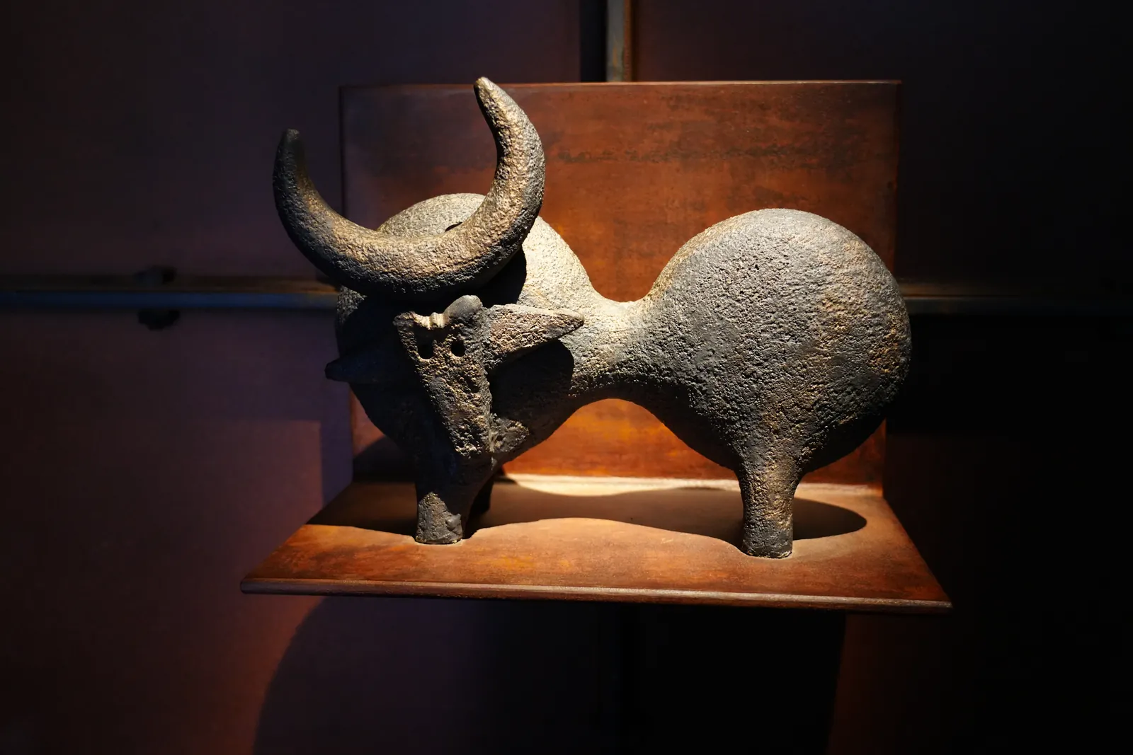 Stone bull-shaped olive oil container lit on a rusted steel shelf in the LA Almazara museum
