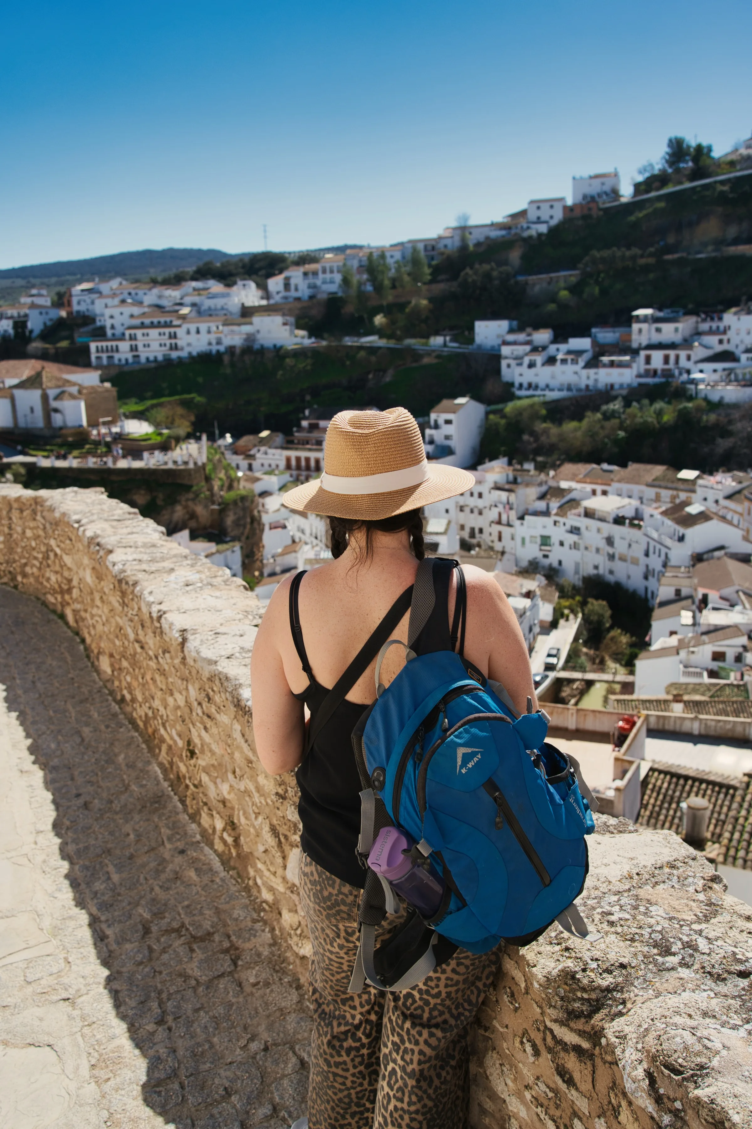 Woman with a backpack looking out over the white rooftops of Setenil de las Bodegas from a high wall