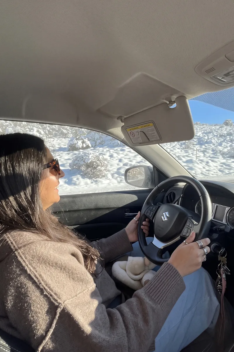 Heidi smiling behind the wheel, driving through the snowy Sierra Nevada