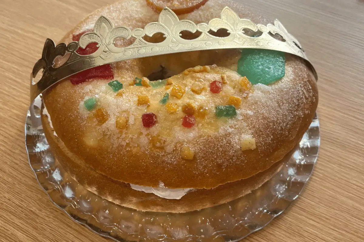 Roscon de Reyes ring cake topped with a paper crown and candied fruit on a glass plate