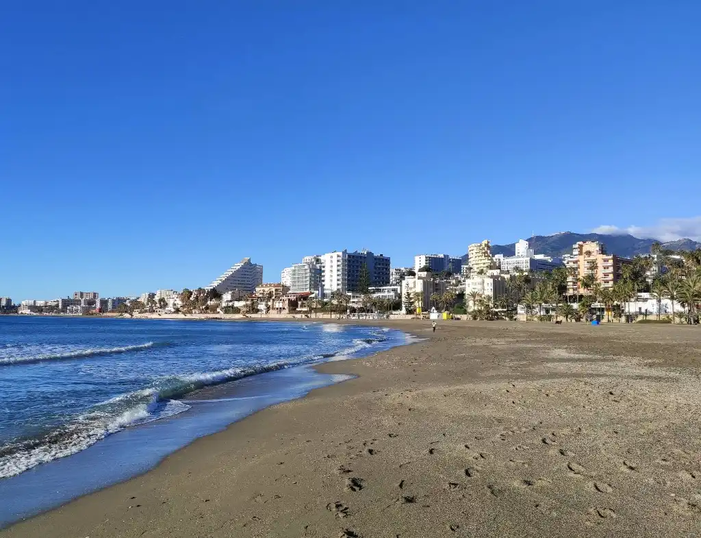 Playa Arroyo de la Miel beach with dark sand, blue sky and apartment buildings behind