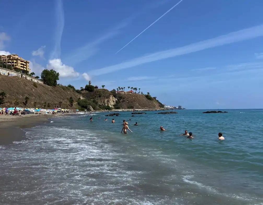 People swimming at Playa Carvajal with a rocky headland and blue water in Benalmadena