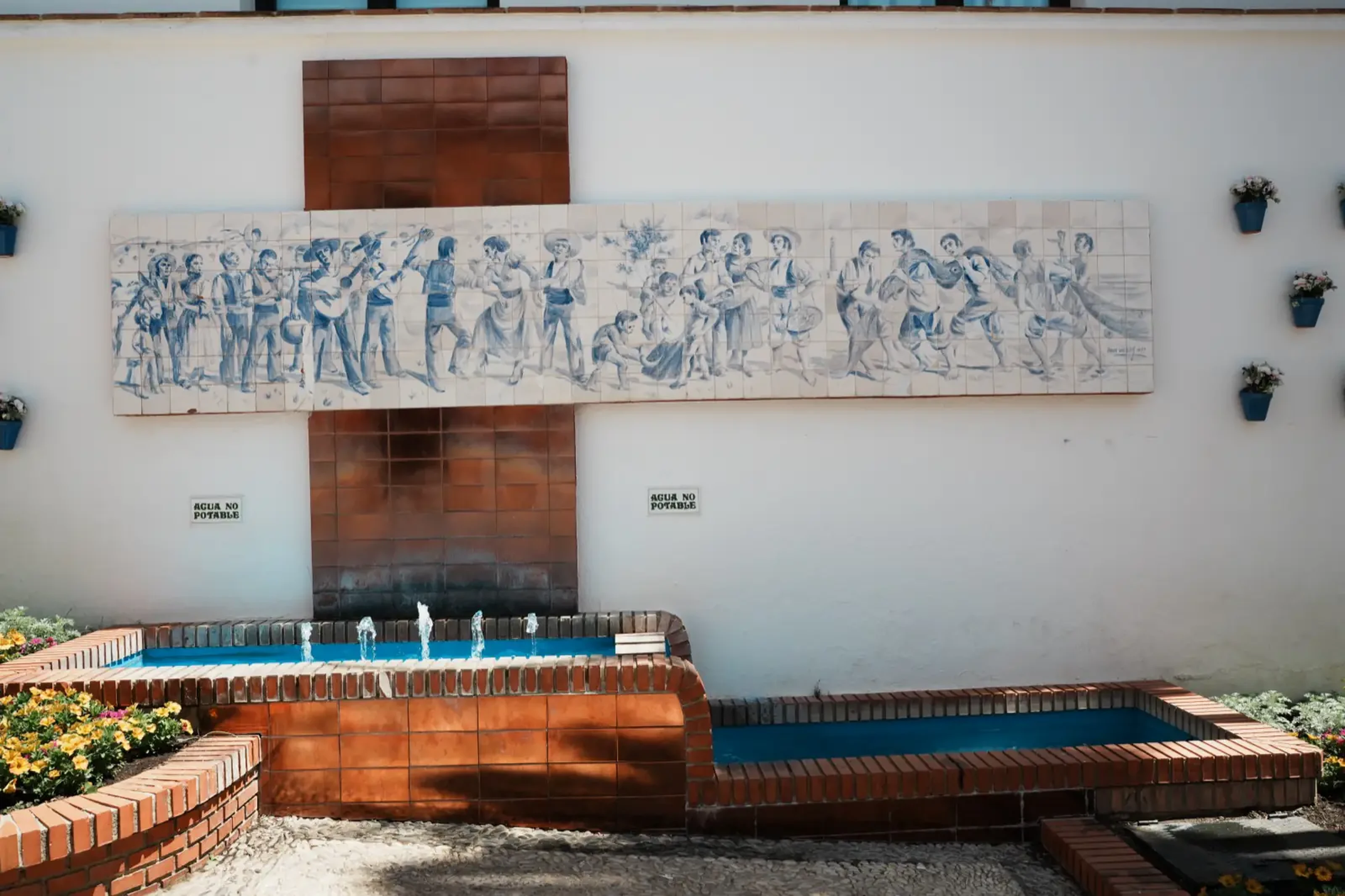 The tiled mural fountain in Plaza Andalucía, Benalmadena Pueblo, with blue flower pots on the wall above