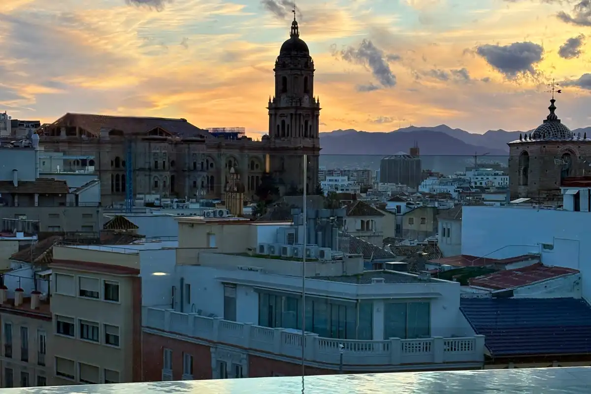 Malaga Cathedral tower rising above the old town rooftops at sunset, seen from the ME Málaga terrace, with the mountains behind