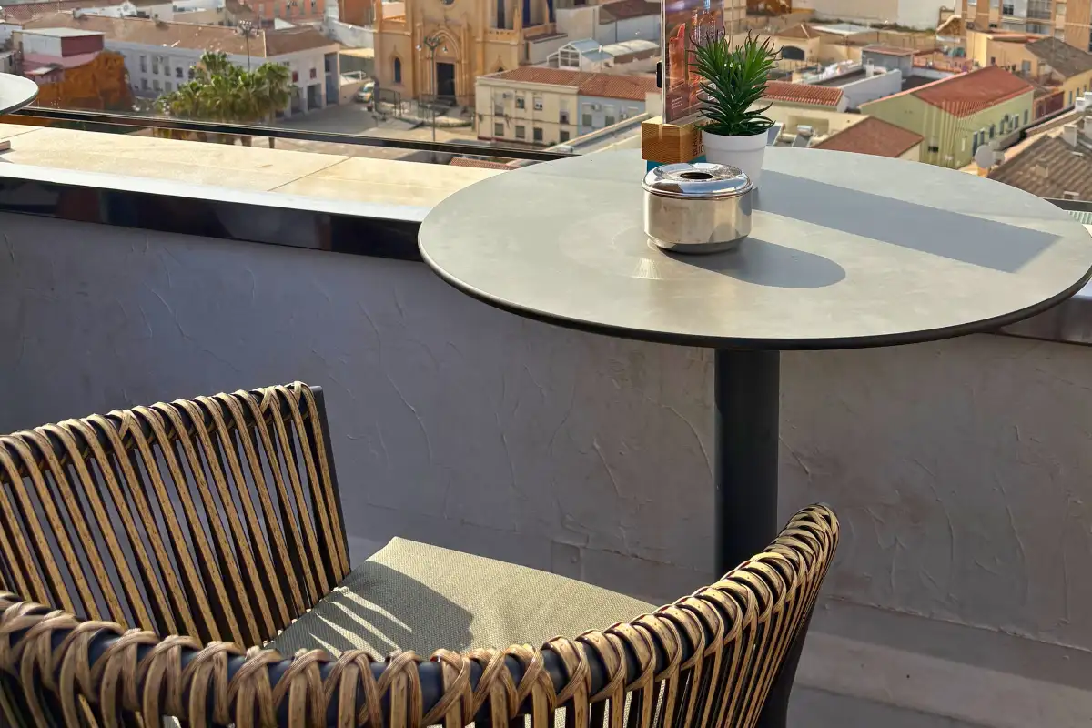 A rattan chair and table on the Aurea rooftop terrace edge, with the Malaga old town rooftops and Gibralfaro Castle visible on the hillside behind