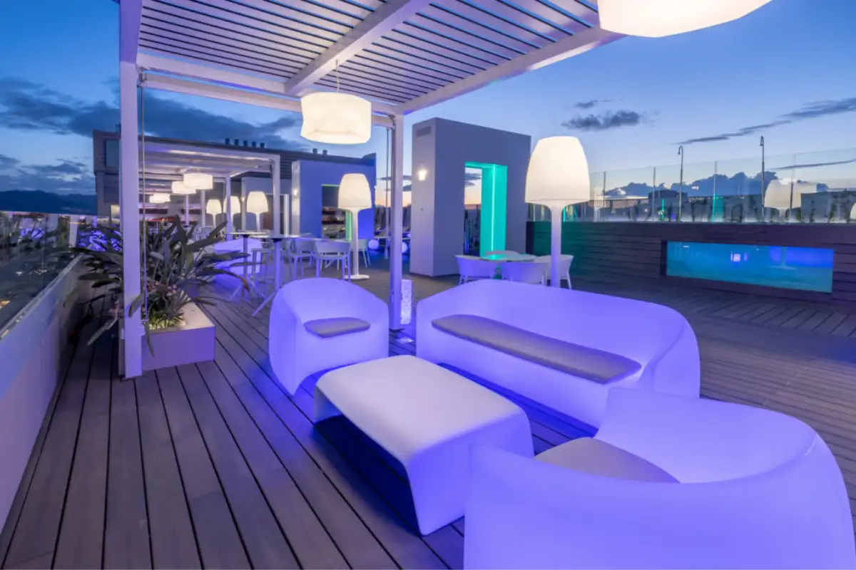 B-Heaven rooftop bar on the Barceló hotel at dusk, with glowing white pod sofas lit in blue and purple and the Malaga skyline behind