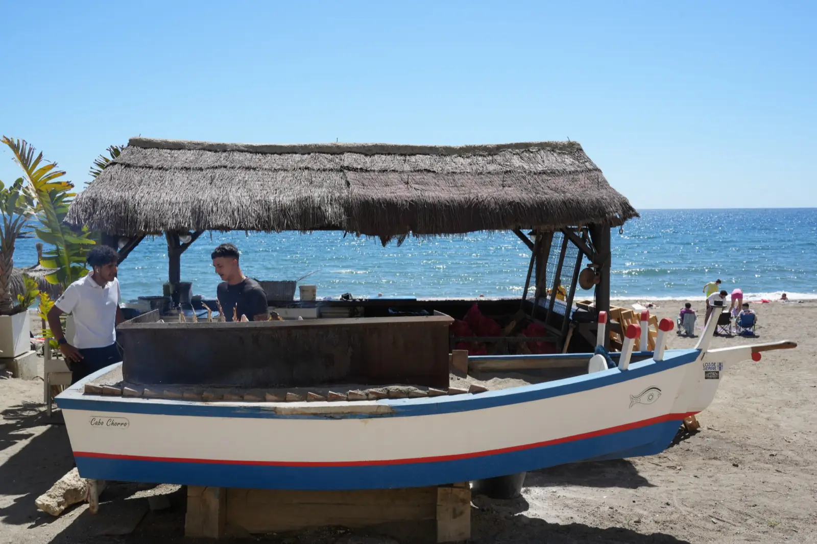 Fishing boat on La Malagueta beach with sardines grilling over a wood fire