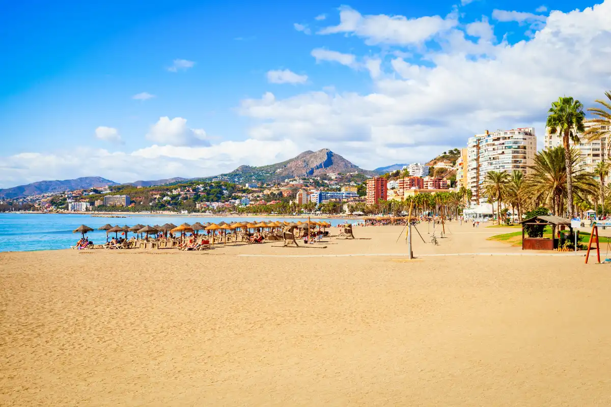 La Malagueta beach in Málaga on a sunny day with sunbeds, palm trees and mountain backdrop