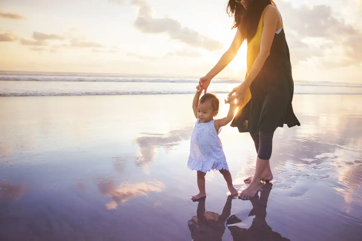 Mother helping her toddler walk on a Málaga beach at sunset