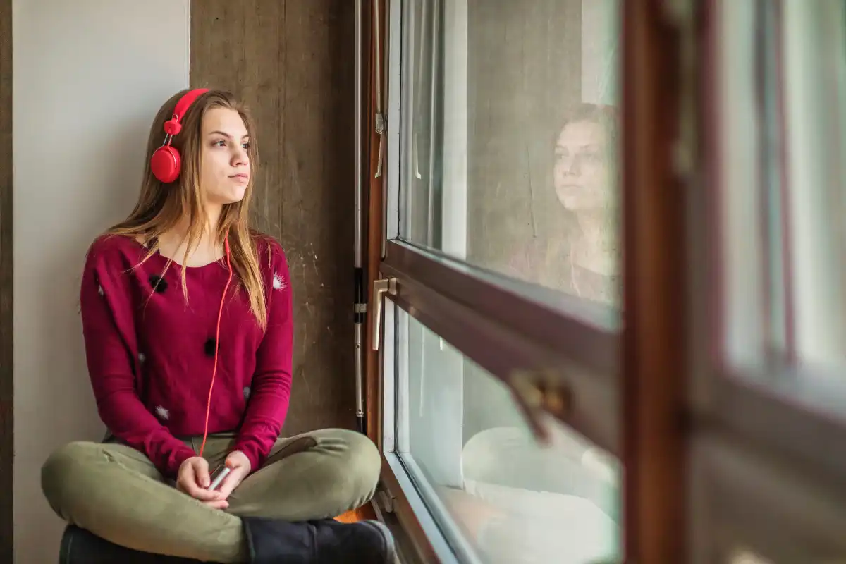 Teenage girl with red headphones sitting by a window