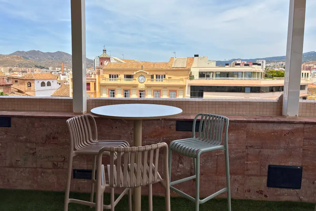 A baroque church bell tower seen from the Larios Terrace rooftop in Malaga, with the glass terrace balustrade in the foreground