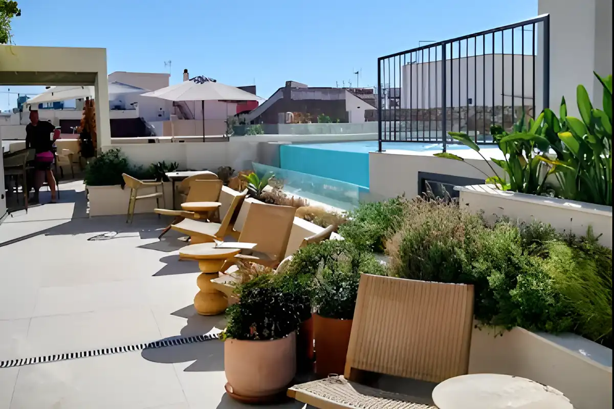 Sunlit rooftop terrace at Well & Come Malaga, with modern ochre chairs, terracotta plant pots, and the pool visible behind a glass barrier