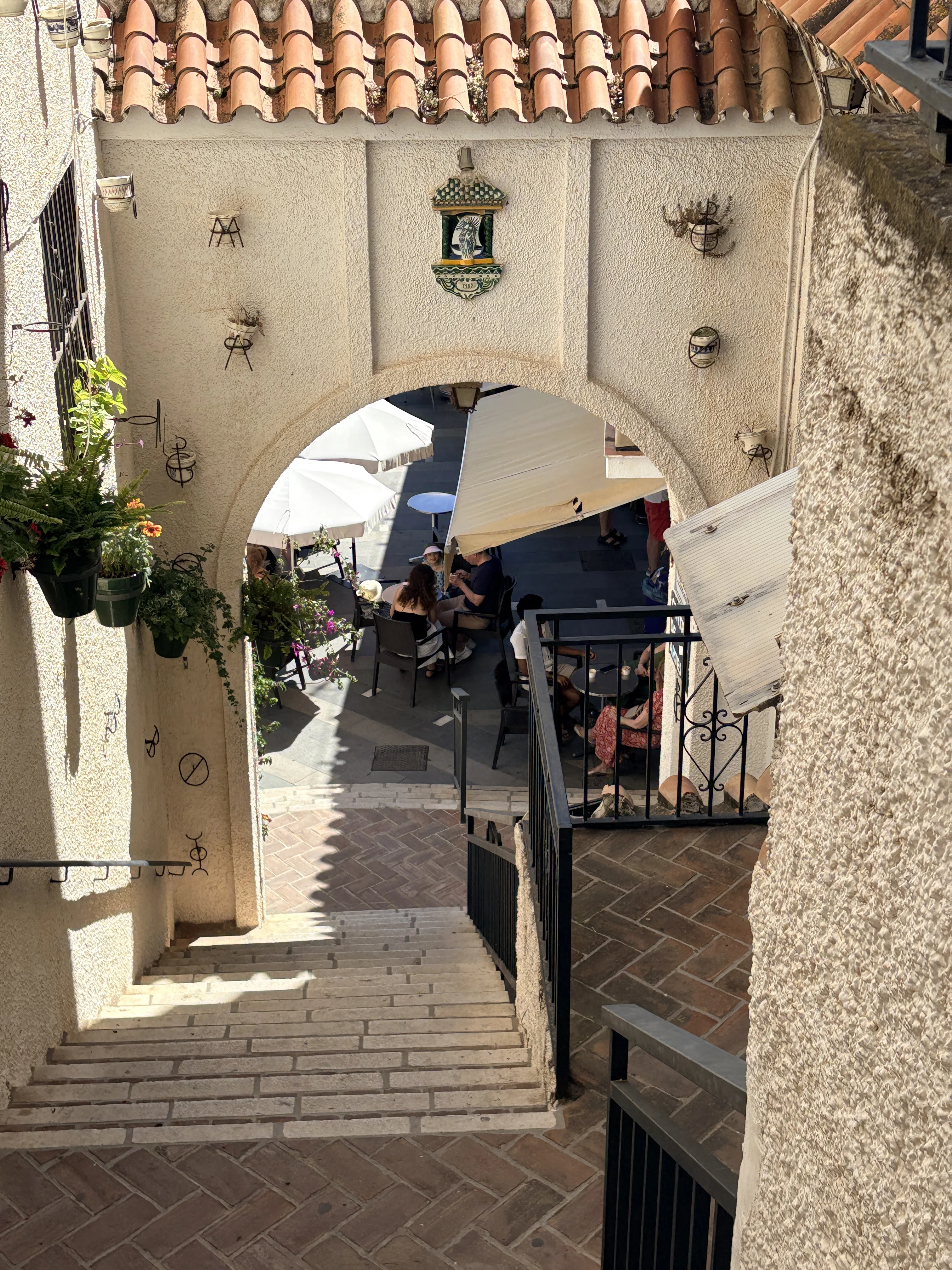 Aerial view looking down through a stone arch into a sunlit courtyard restaurant in Mijas