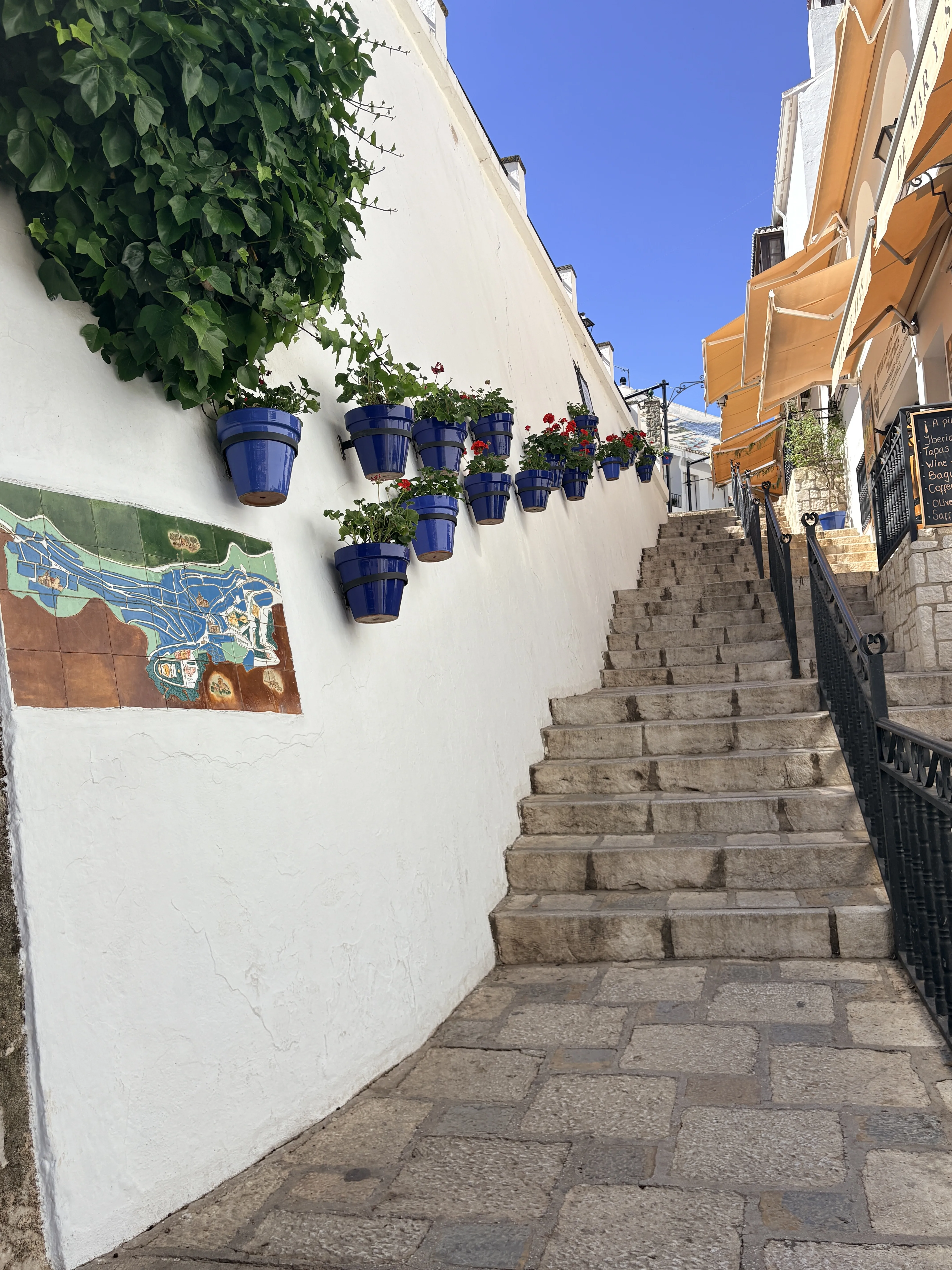 Blue flower pots hanging on a white wall beside a café awning in Mijas village
