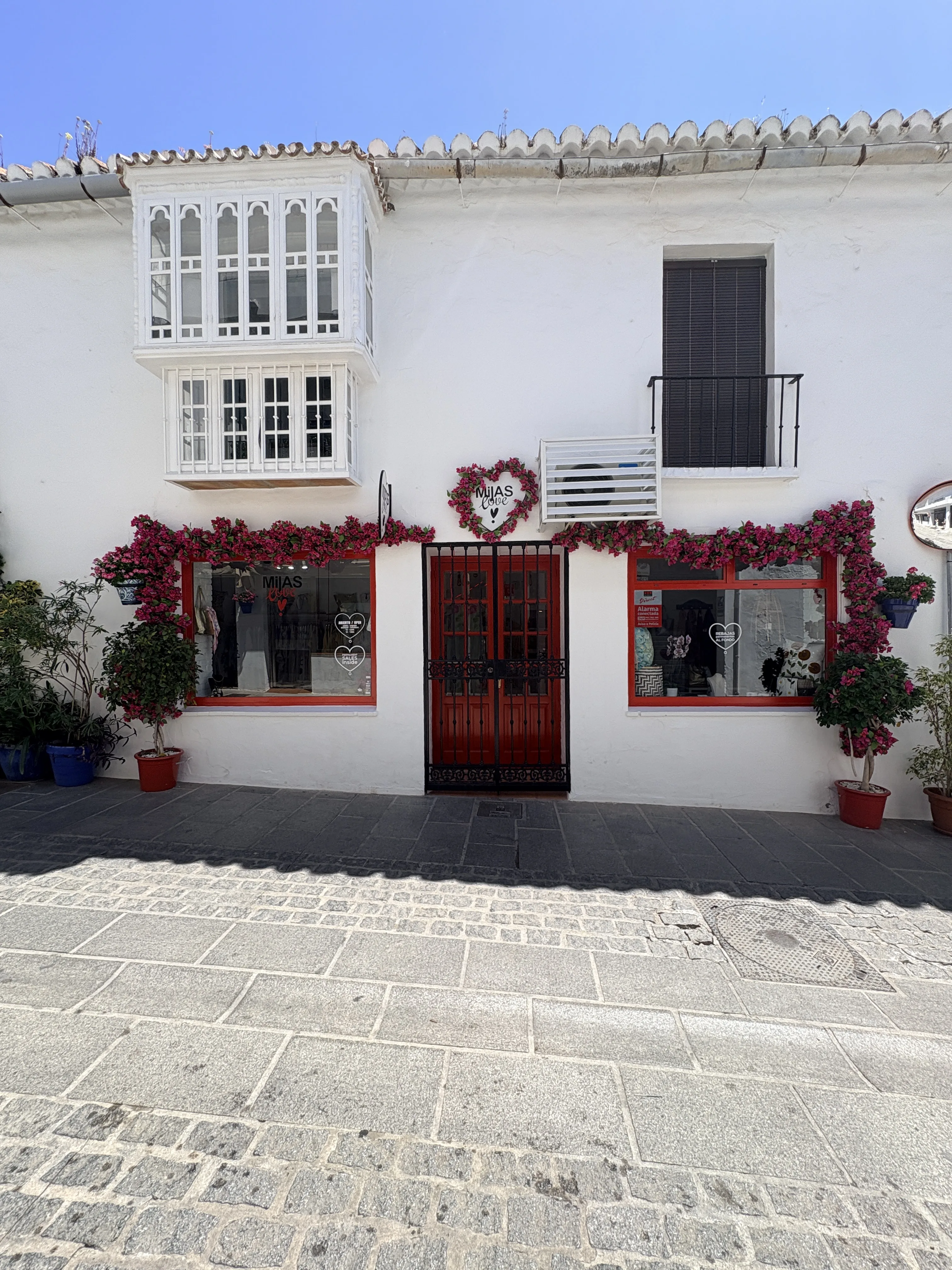 White building with red window frames covered in geraniums in Mijas