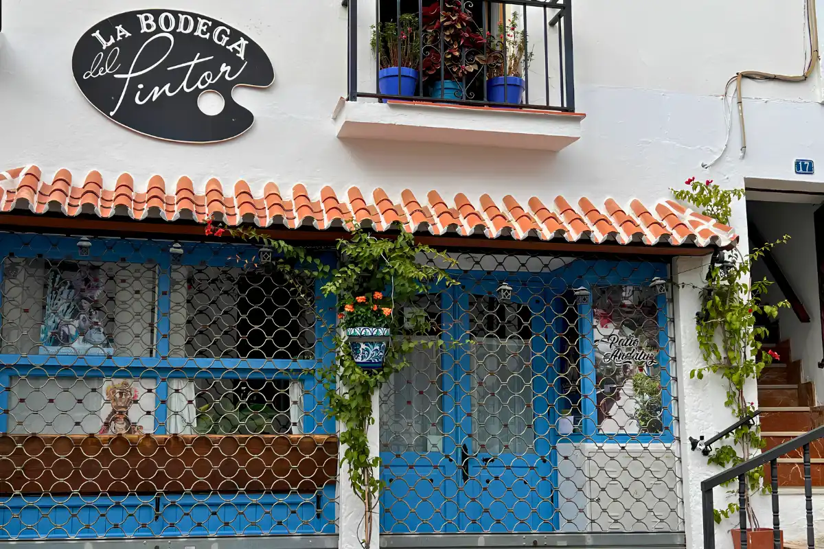 The exterior of La Bodega del Pintor in Mijas Pueblo with its distinctive black oval sign and blue shuttered windows