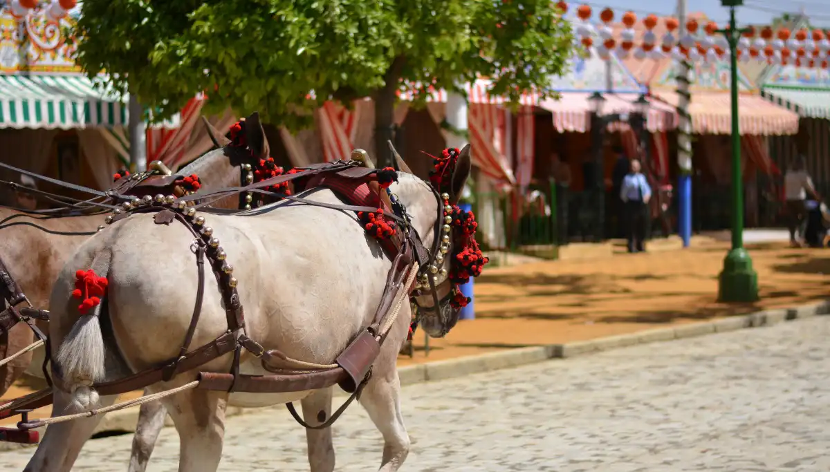 White horses pulling carriage past striped caseta tents at Feria de Abril