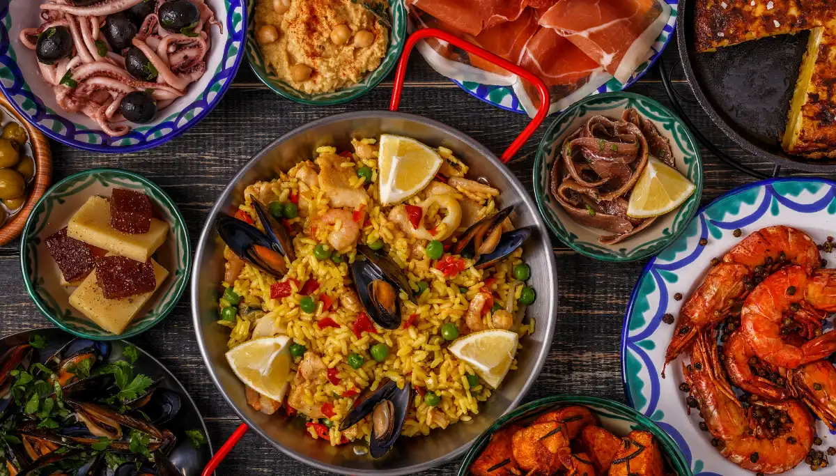 Spread of Spanish tapas including paella, prawns, and cured ham