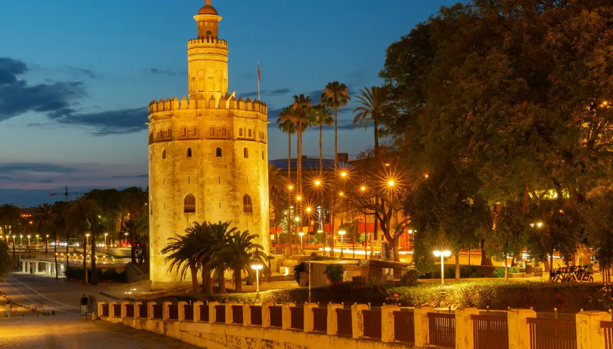 Torre del Oro illuminated at night with palm trees along the riverbank